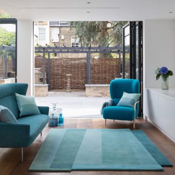 Sonya Winner Aqua Teal Sea rug shown in an elegant modern living room, with turquoise armchair and sofa and blue, geometric cushions