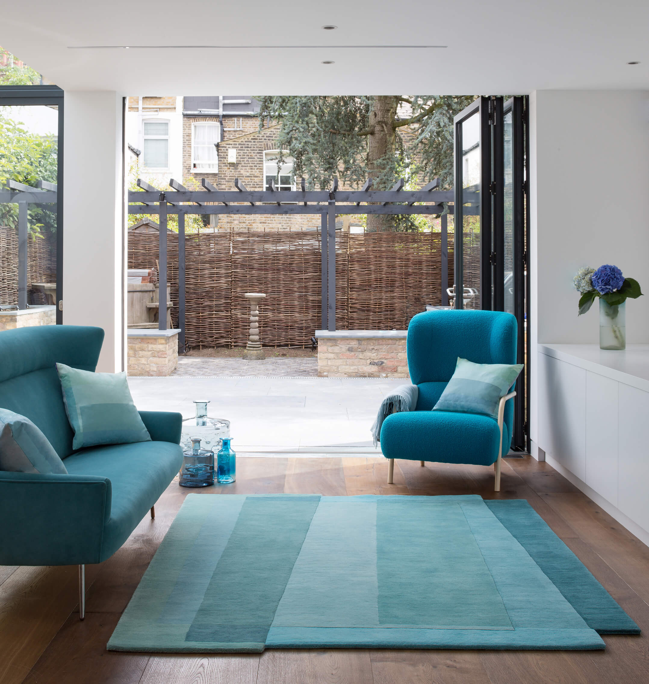 Sonya Winner Aqua Teal Sea rug shown in an elegant modern living room, with turquoise armchair and sofa and blue, geometric cushions