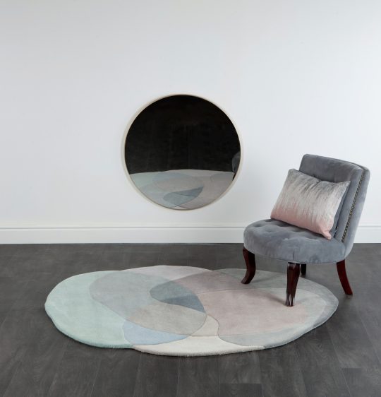 Sonya Winner Jellybean Coconut rug, in an elegant monochrome design setting with dark wooden floor, grey velvet armchair and silver satin cushion in front of mirror