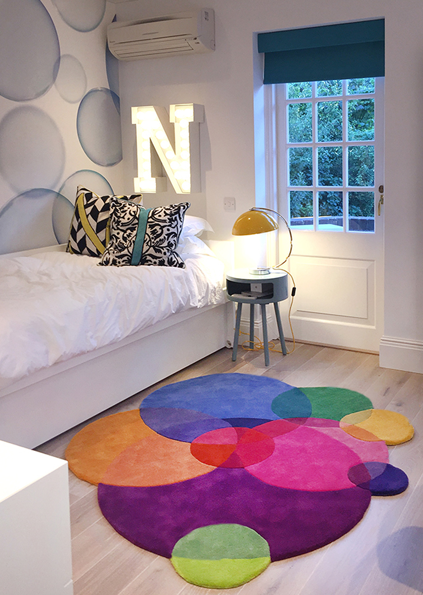 Sonya Winner Bubbles rug shown in a modern colourful kids room with letter lights, yellow bedside lamp and nature patterned cushions